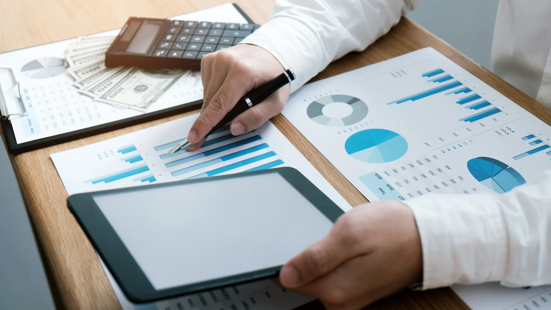 Profissional analisando gráficos financeiros, com tablet, calculadora e dinheiro sobre a mesa, representando a rotina estratégica de escritórios de contabilidade e a importância de presença digital