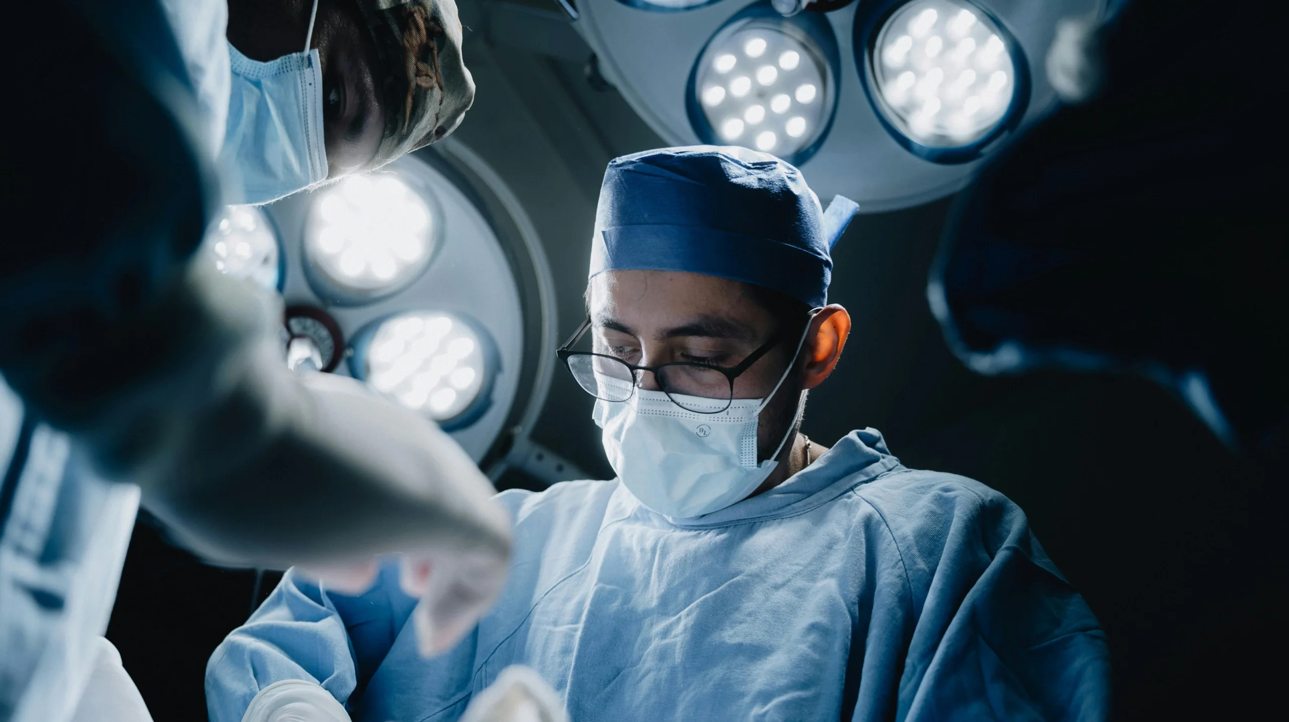 Cirurgião realizando procedimento cirúrgico em centro cirúrgico moderno, utilizando equipamentos médicos e iluminação profissional, representando segurança, precisão e atuação especializada.
